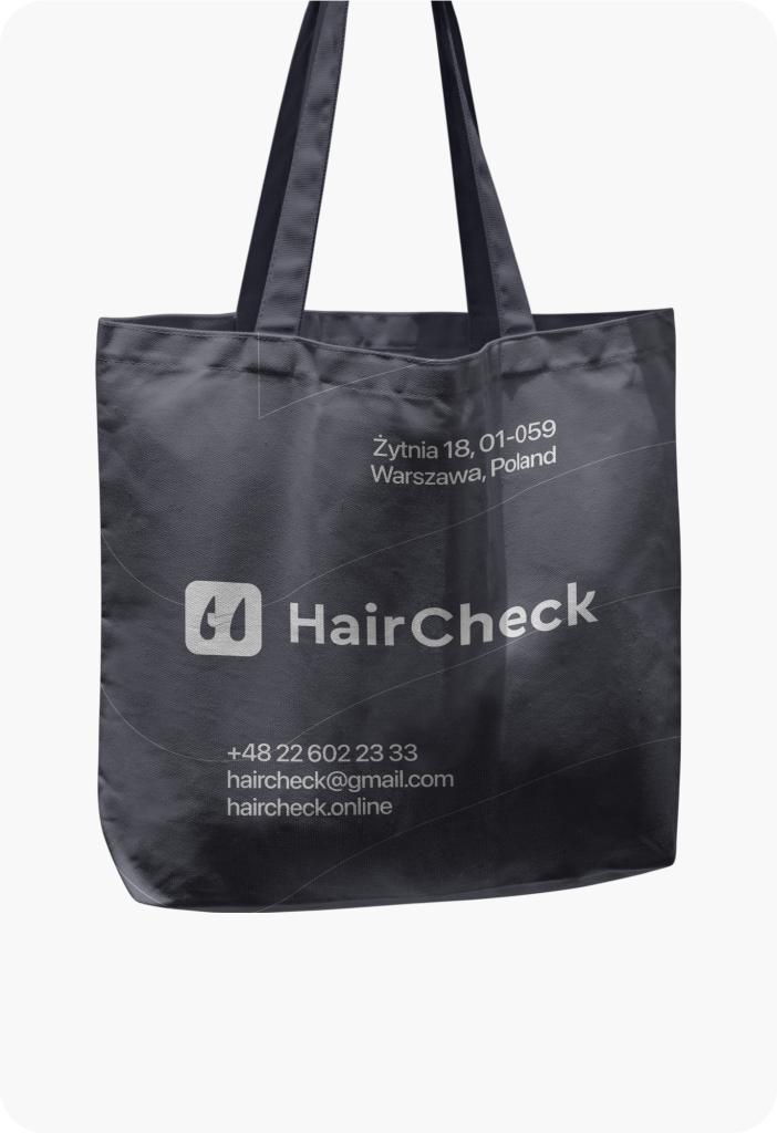 A gray tote bag with the HairCheck logo, contact number, email, and website.